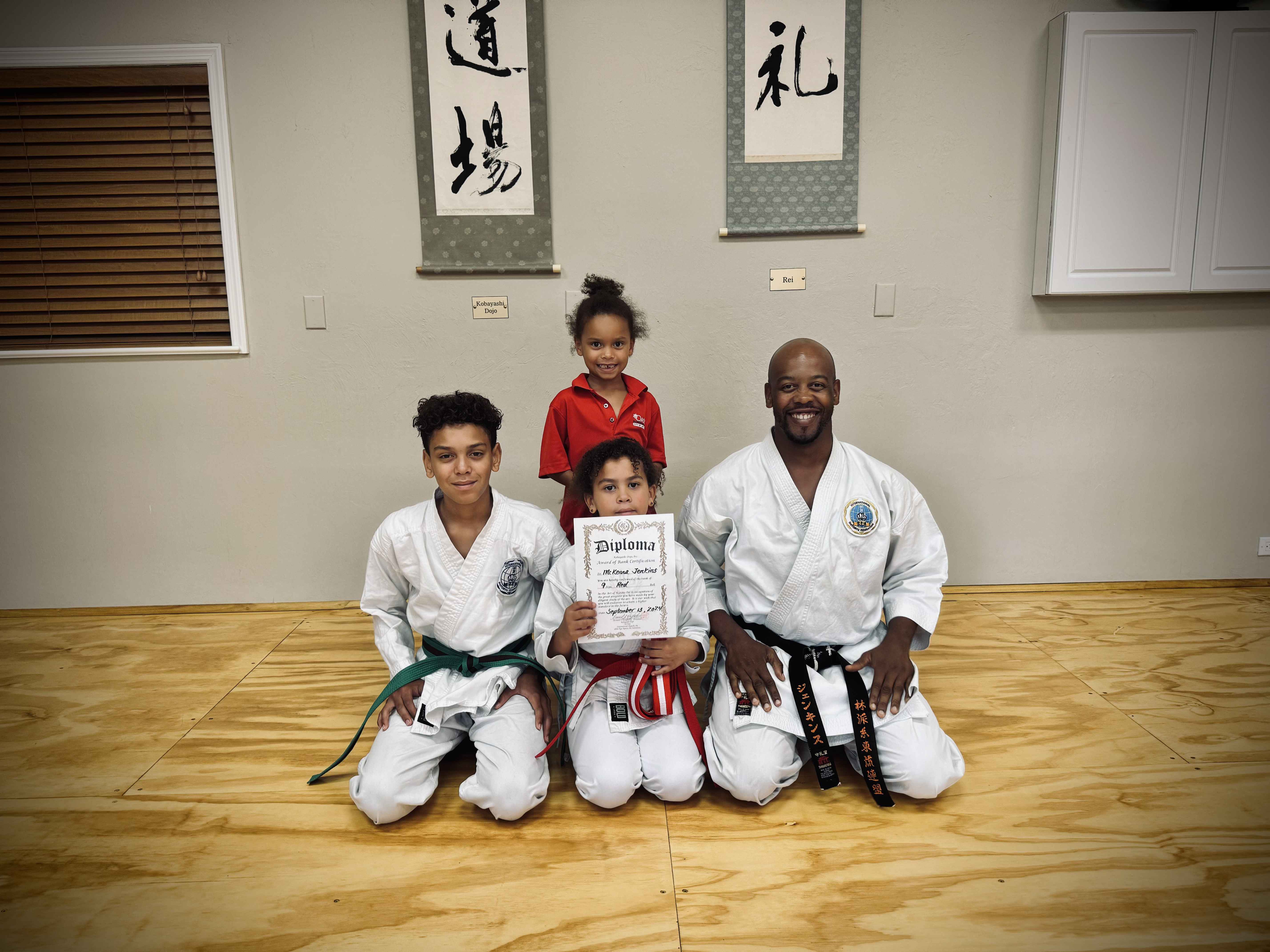 Sensei Jenkins kneeling with his children after a belt promotion