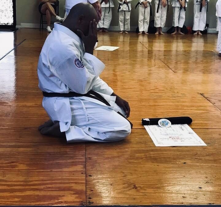 Sensei Jenkins kneeling in seiza beside his belt and rank certificate